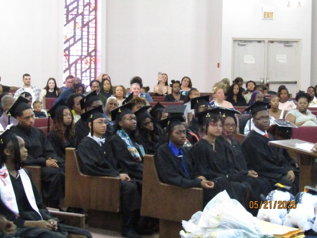 Young adults in graduation caps and gowns sit in pews.