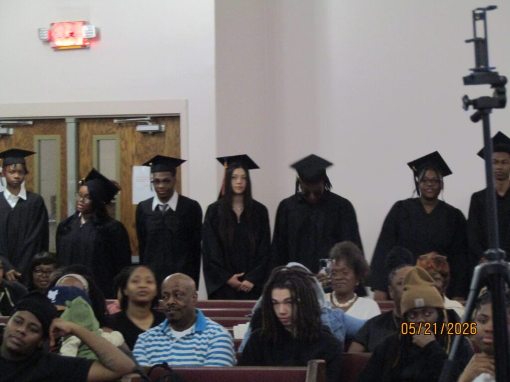 Young adults in graduation caps and gowns with audience members.