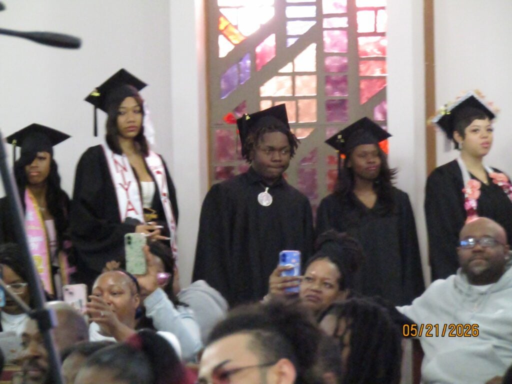 Young adults in graduation caps and gowns with attendees taking photos.