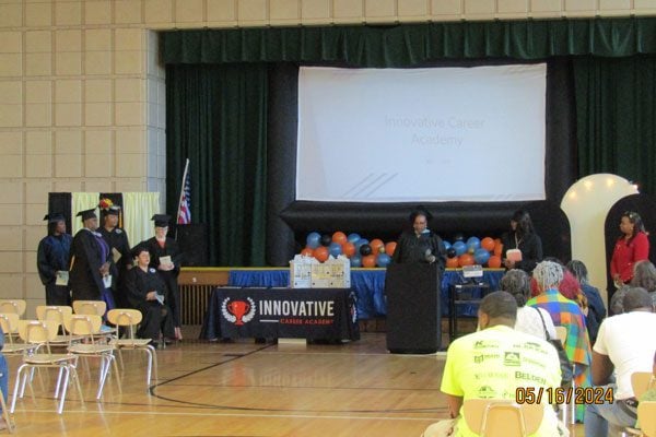 Graduation ceremony with adults on stage and screen showing "Innovative Career Academy."