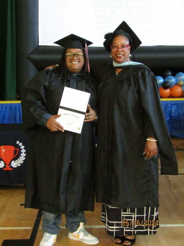 Two adults in graduation caps and gowns, one holding a diploma.