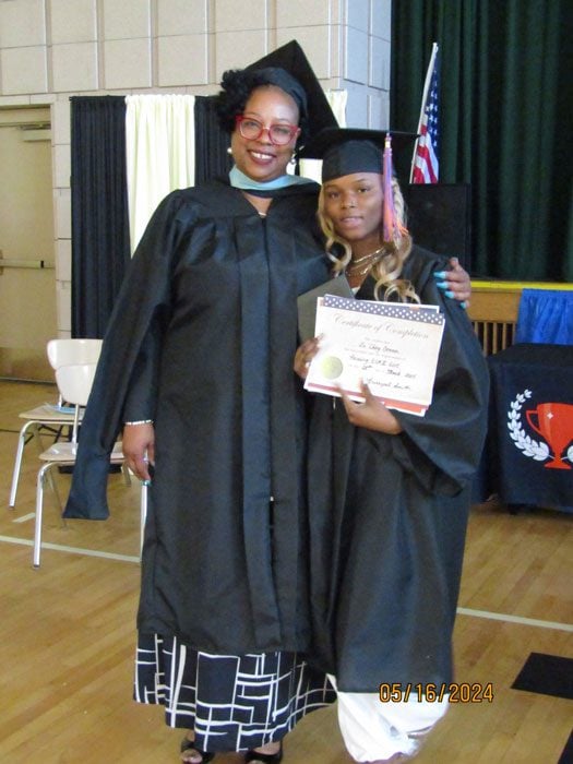 Two adults in graduation attire, one holding a certificate.