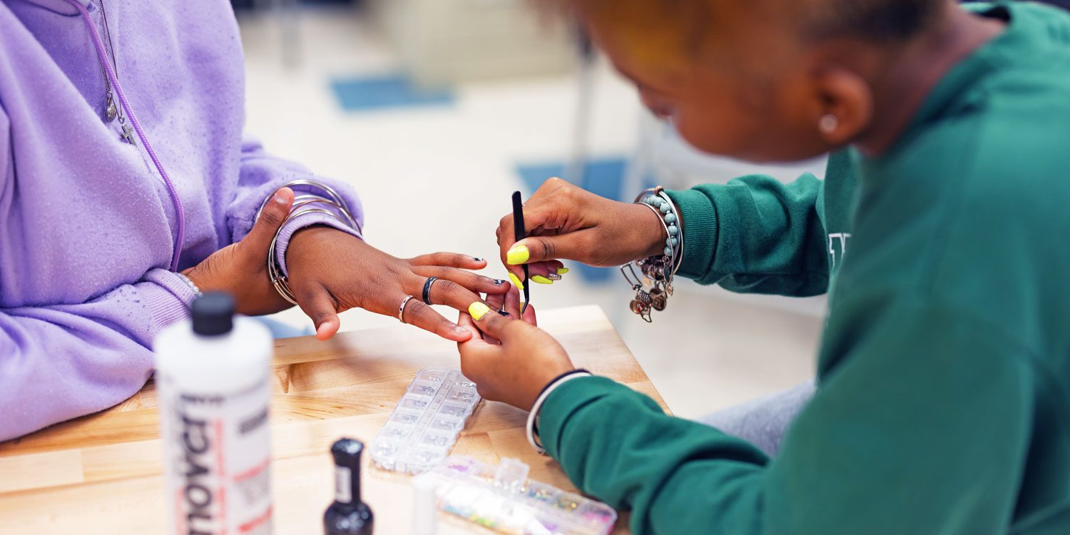 Close-up of one person applying nail polish to another person's nails at a table.