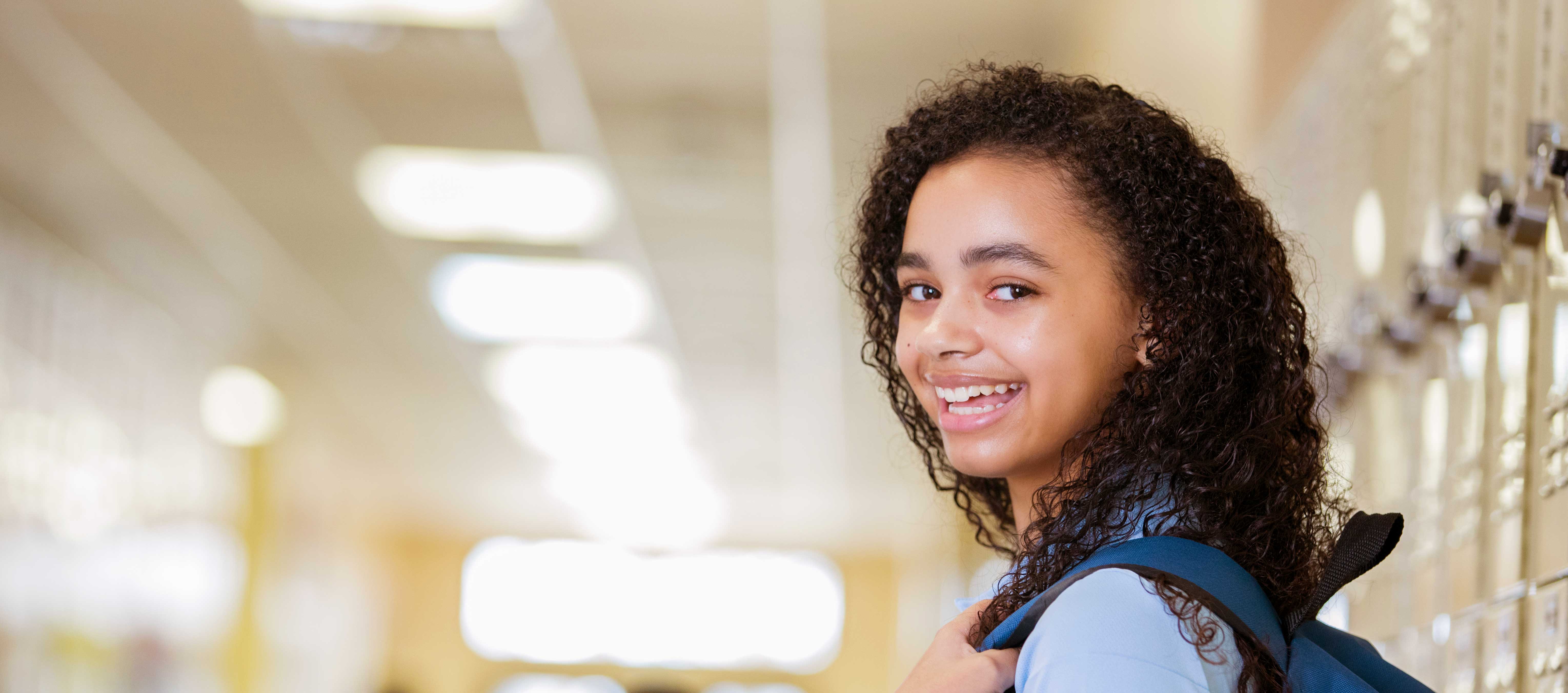 High School student with a backpack smiling in hallway.