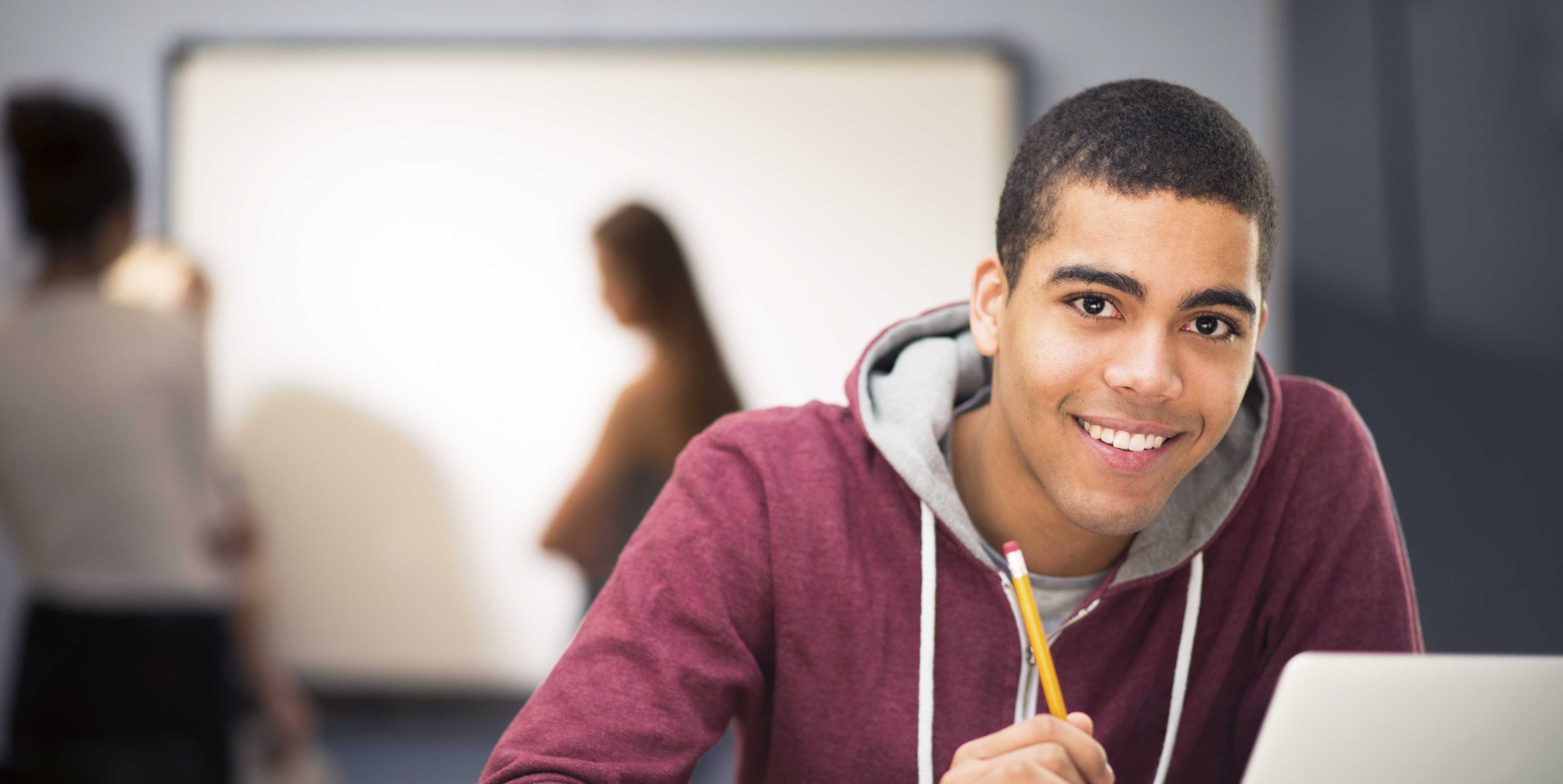 Smiling high school student holding pencil and working on a laptop.